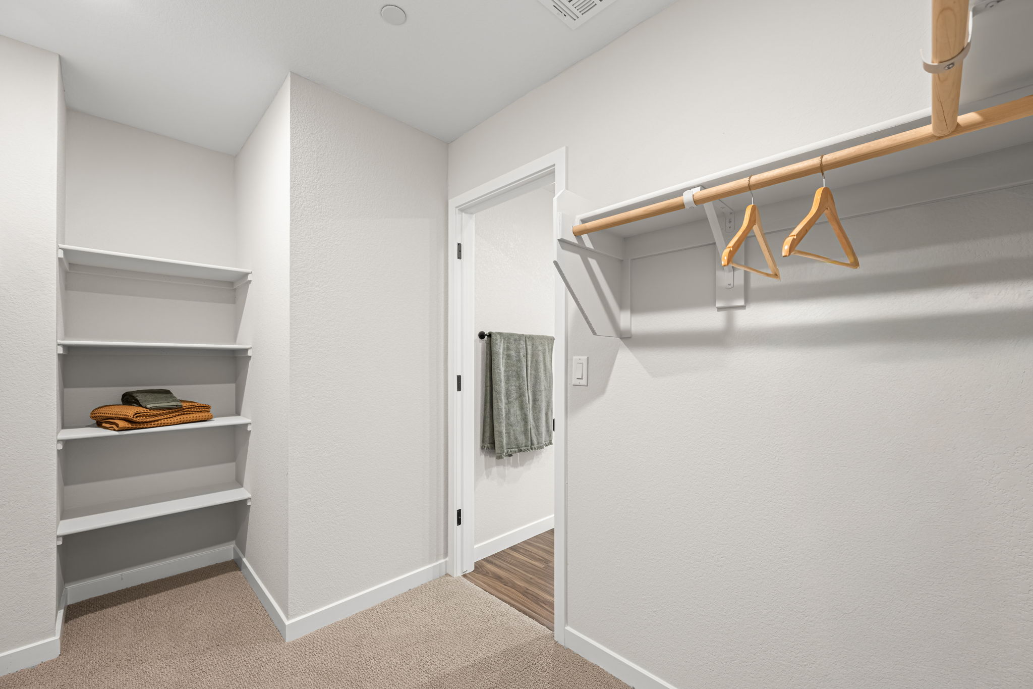 A white room with a white door and a white shelf with a towel from it.