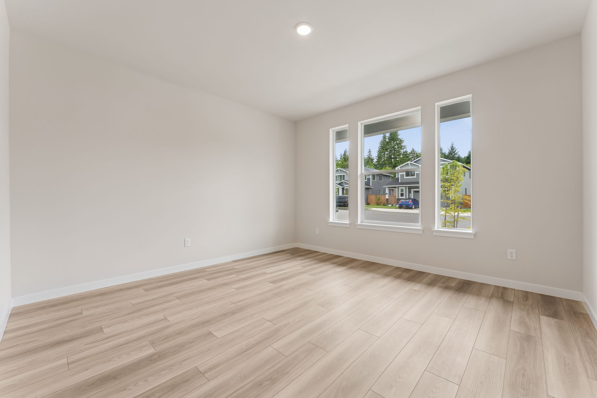 A room with a wood floor and a window with a view of a street and trees.